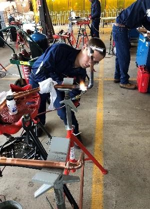 A welder bent over focused on welding copper joints